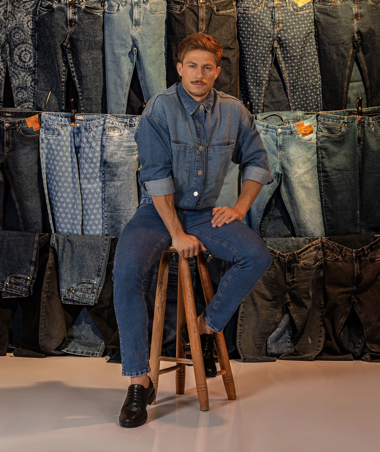 Modelo sentado em um banco, com camisa e calça jeans